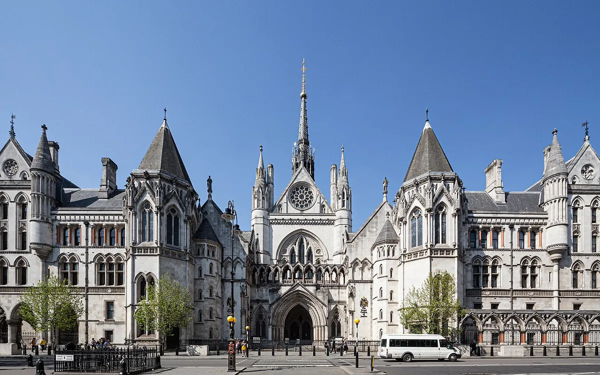 The Gothic stone front of the Royal Courts of Justice on the Strand in London, its spired main gate under a clear blue sky